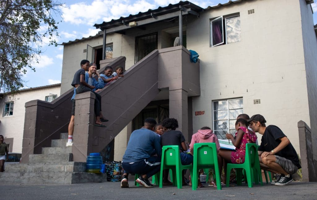 Stijn and Little Lions coaches hosting a workshop at one of the local houses. The children are sitting around a plastic table completing their activities.