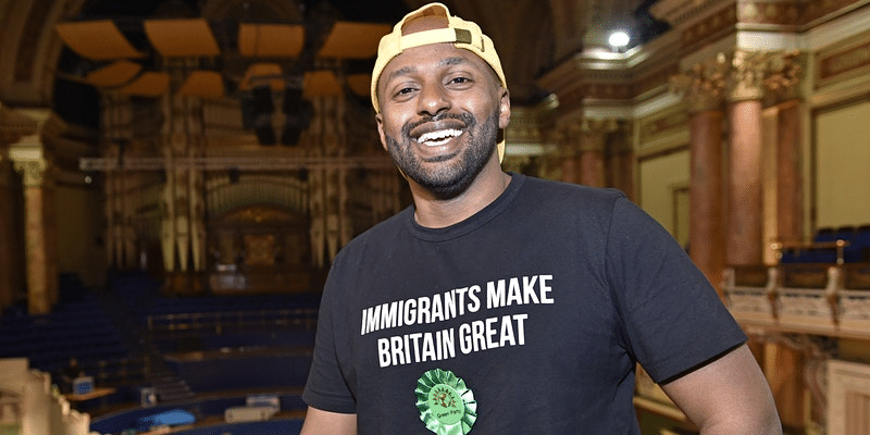 Event poster of Magid Magid smiling in a black "immigrants make Britain great " t-shirt.
